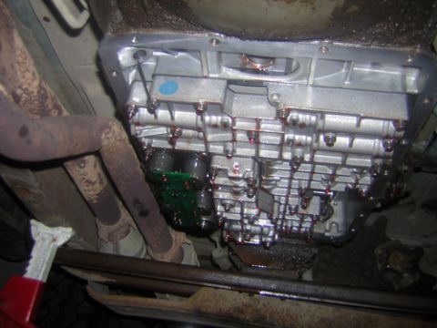1995 Ford Bronco - Underside view of a transmission pan with a drain plug and signs of fluid leakage.