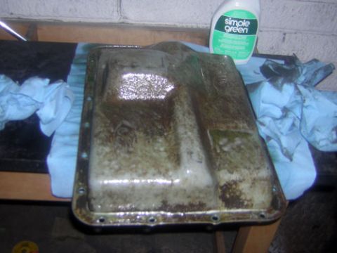 1995 Ford Bronco - A transmission oil pan sits on a workbench next to a bottle of Simple Green cleaner and some rags.