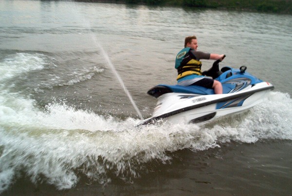 Man riding a blue and white Yamaha jet ski on the water, spraying wake.