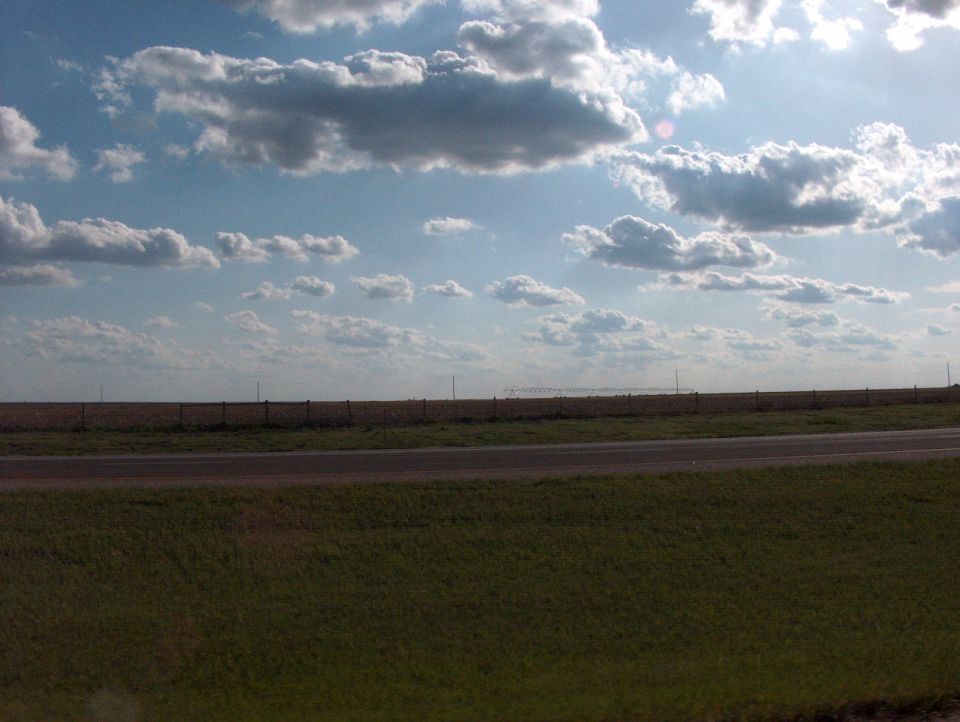 Wide sky with clouds over a flat landscape with a road and grass