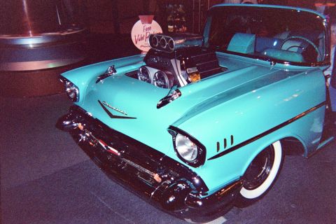 1968 Ford Mustang - A heavily modified 1957 Chevrolet Bel Air convertible, a large supercharger and custom paint, is displayed indoors.