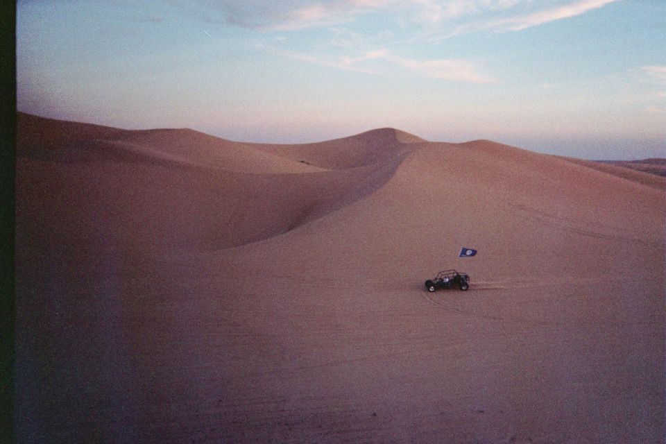 Dune buggy with blue flag driving on sand dunes at sunset