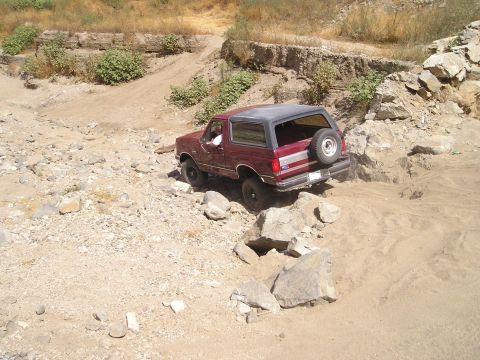 1989 Ford Bronco - A maroon Ford Bronco tackles a challenging off-road course with rocky terrain.