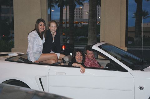 1994 Ford Bronco - People ride in a white convertible with palm trees and buildings in the background.