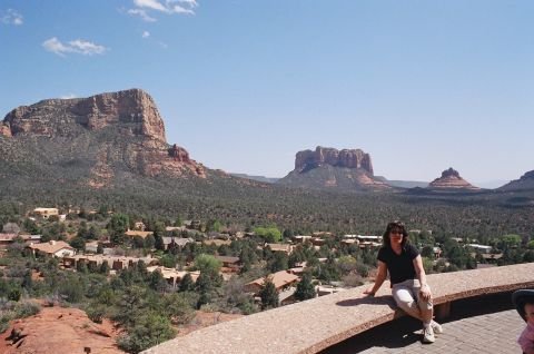 1994 Ford Bronco - A woman kneels on a stone ledge overlooking a town among red rock formations under a clear blue sky.