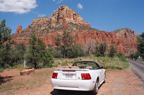 1994 Ford Bronco - A white convertible Mustang is parked on a dirt road with a scenic view of red rock formations under a blue sky.