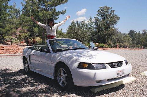 1994 Ford Bronco - White convertible Mustang parked outside with a person standing up in the driver's seat.