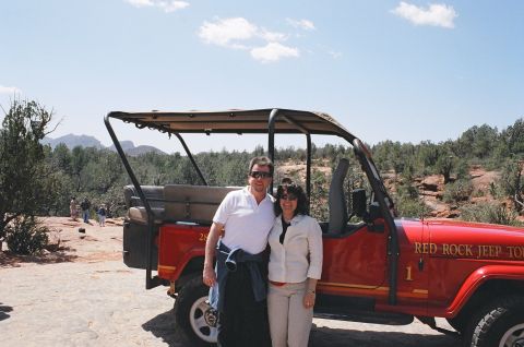 1994 Ford Bronco - A couple stands next to a red jeep tour vehicle in a rocky, arid landscape under a clear blue sky.