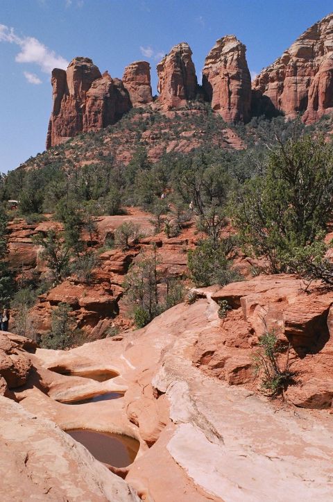 1994 Ford Bronco - A scenic view of towering red rock formations under a clear blue sky, with a winding path and water-filled depressions in the foreground.