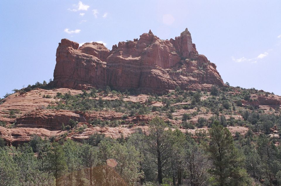 Red sandstone butte with spires above juniper and pine trees under a blue sky