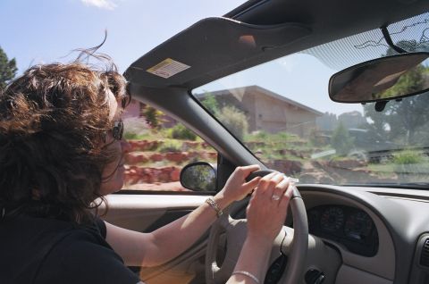 1994 Ford Bronco - A woman drives a car through a scenic, arid landscape under a bright blue sky.