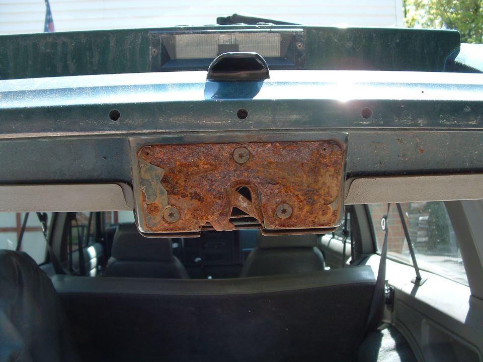 Rusty rear hatch latch mechanism on a dark green vehicle