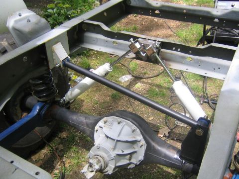 1978 Ford Bronco - A bare ladder frame during a chassis build, showing a freshly painted front solid axle with center differential, coil springs, radius arms,…