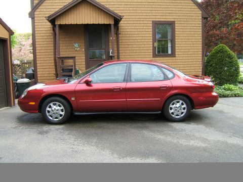 1998 Ford Taurus - Side profile of a red 1998 Ford Taurus sedan parked on a paved driveway.