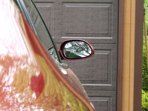 1998 Ford Taurus - Side mirror of a red vehicle reflects trees and sky, parked in front of a garage door.