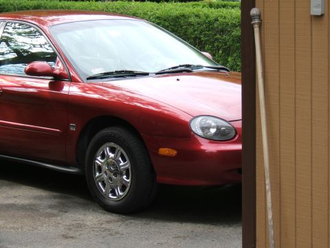 1998 Ford Taurus - The front quarter panel and headlight of a red 1998 Ford Taurus are visible.