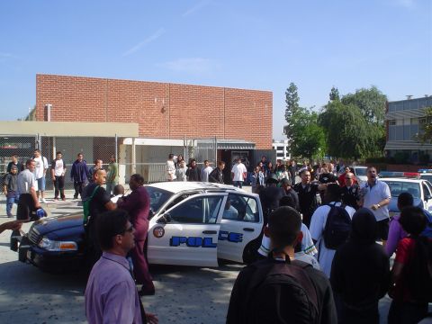1993 Ford Taurus - A group of people are gathered around police vehicles outside a brick building on a sunny day.