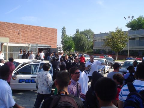 1993 Ford Taurus - A crowd of people, including police officers, are gathered around police cars in front of a brick building.