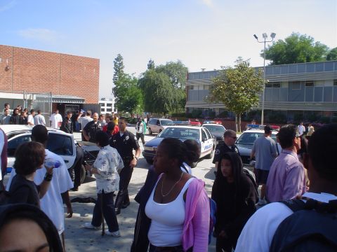 1993 Ford Taurus - A group of people and police officers are gathered in front of a school building on a sunny day.