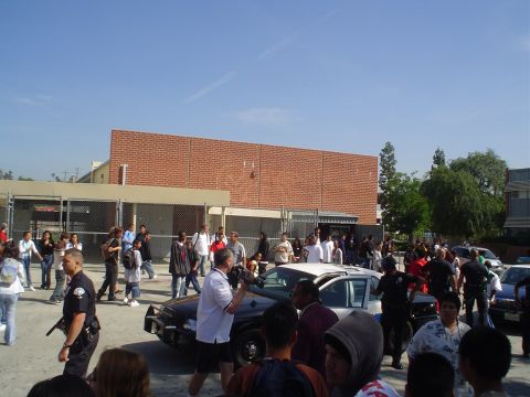 1993 Ford Taurus - A police car is surrounded by a crowd of people in front of a brick building under a clear blue sky.