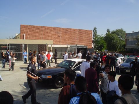 1993 Ford Taurus - A police car is present at a gathering of people outside a brick building.