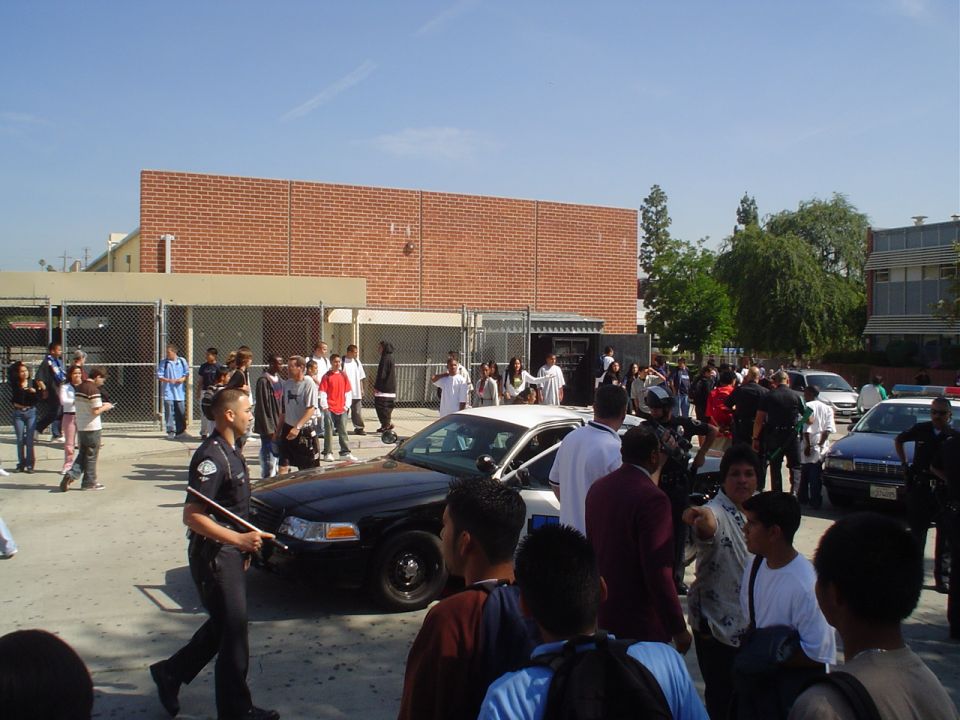 Black and white police car parked on asphalt, with a crowd of people gathered around
