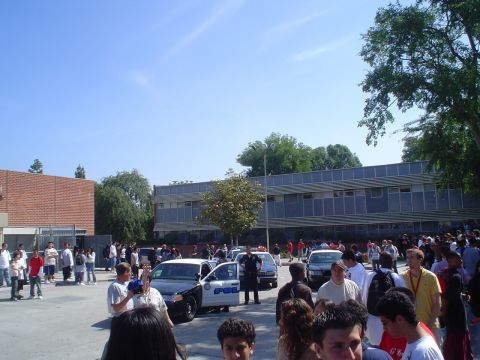 1993 Ford Taurus - A gathering of people surrounds police vehicles in a school parking lot.