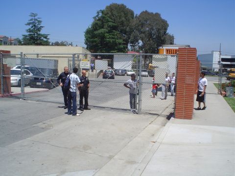 1993 Ford Taurus - Several vehicles and individuals are visible behind a fence, with a sign indicating 'Gates Must Be Locked When Not In Use'.