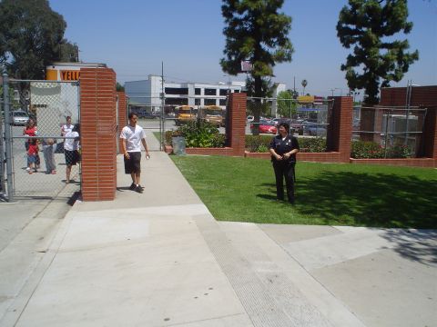 1993 Ford Taurus - A police officer stands guard at a school entrance, with people visible through the fence.