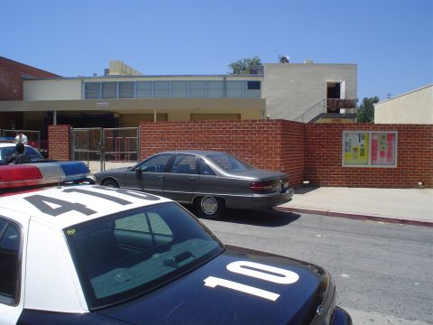 1993 Ford Taurus - Two police cars and a sedan are parked on a street in front of a building with a brick wall.