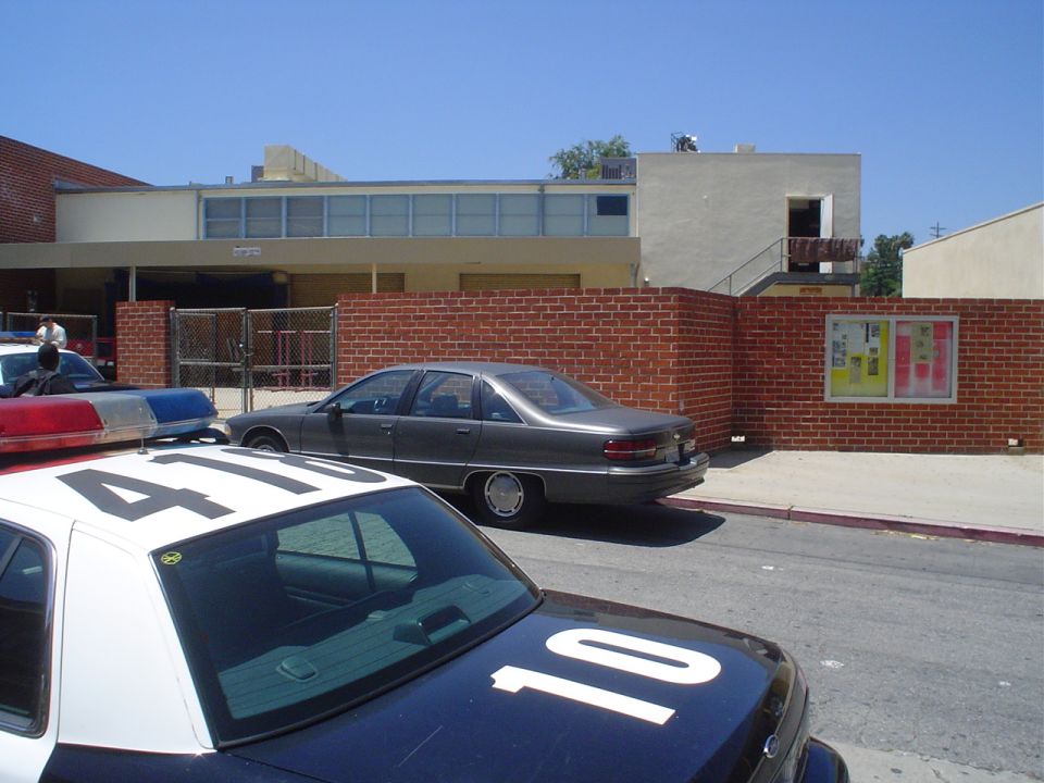 Police car with '4110' on roof parked next to a gray sedan in front of a brick wall and building