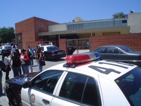 1993 Ford Taurus - Multiple police vehicles are present outside a building with a brick facade and a group of people gathered.