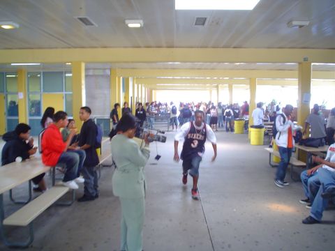 1993 Ford Taurus - A busy school hallway scene with students gathered and a person filming with a video camera.