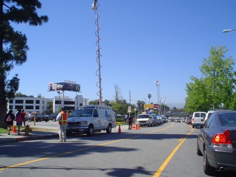 1993 Ford Taurus - A white van equipped with a tall antenna tower is parked on the side of a road, with other vehicles in the background.