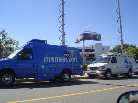 1993 Ford Taurus - Two broadcast news vans are parked on the street, one blue and one white, under a clear sky.