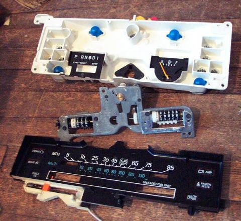 1985 Ford Crown Victoria LTD - Disassembled dashboard gauges, including the odometer and fuel gauge, are laid out on a wooden surface.