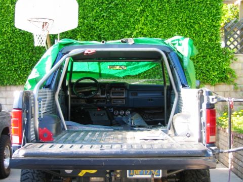 1985 Ford Bronco - Interior view of a 1985 Ford Bronco, modified with a roll cage and covered with a green tarp.
