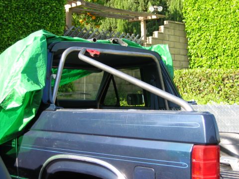 1985 Ford Bronco - A custom roll cage is visible in the bed of a pickup truck, with a green tarp covering part of the vehicle.
