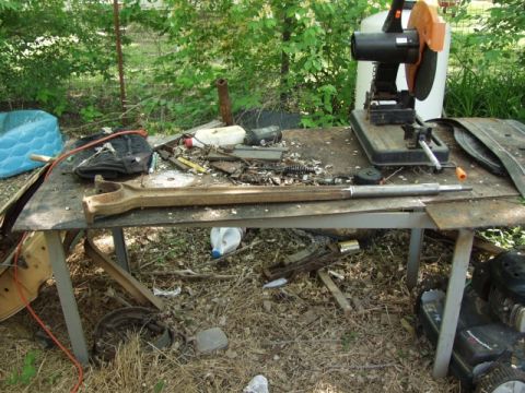 1979 Ford Bronco - A cluttered workbench holds a metal cutting saw, various tools, and a large, rusty metal component.
