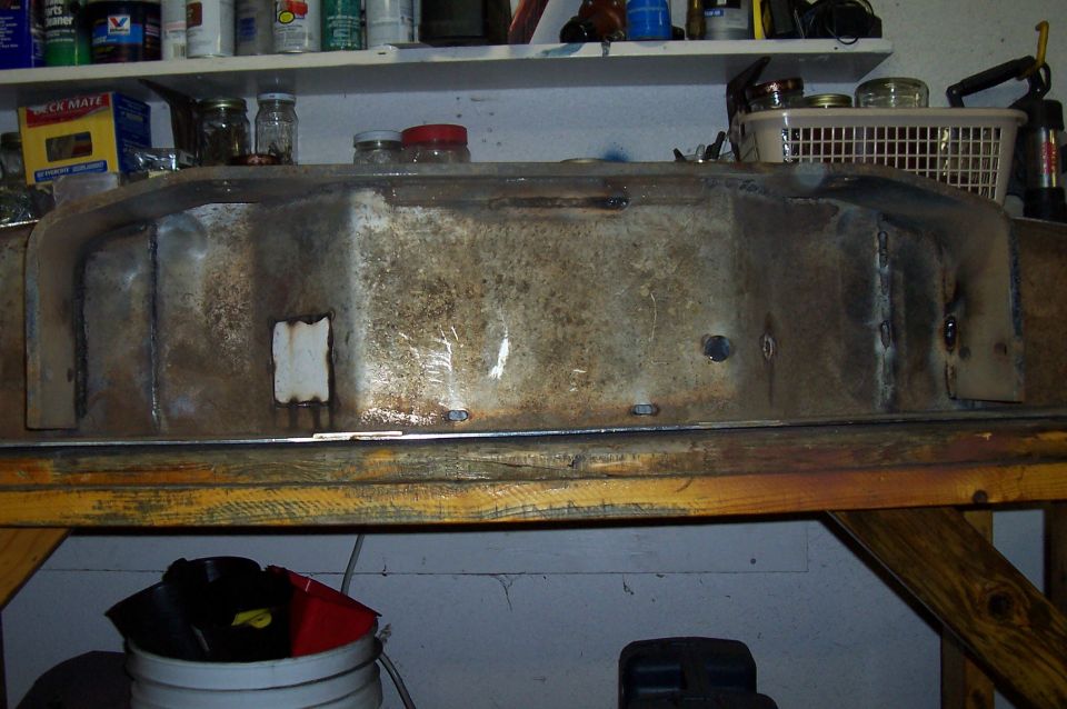 Welded metal fuel tank with some rust and patches, resting on a wooden workbench