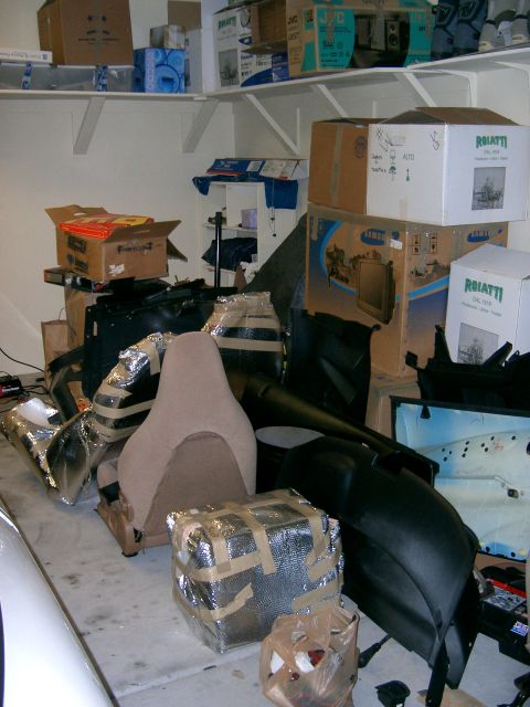 1996 Ford Probe - Various car parts, including a seat and fender, are stored in a garage with boxes on shelves.