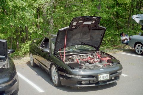 1995 Ford Probe - A black 1995 Ford Probe is parked with its hood open, revealing the engine bay. Another vehicle is partially visible to the left, and a per…