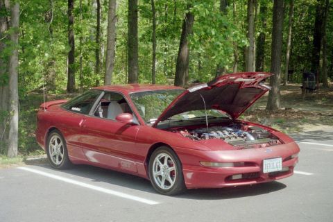 1995 Ford Probe - A red 1995 Ford Probe is parked with its hood open, revealing the engine, surrounded by trees.