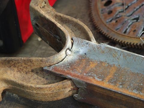 1979 Ford Bronco - Close-up view of heavily rusted metal components, possibly from a vehicle's chassis or drivetrain, with a flywheel visible in the backgroun…