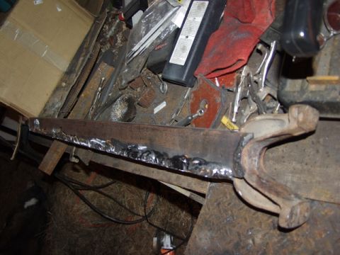 1979 Ford Bronco - A close-up view of a metal component that has been welded, resting on a workbench amidst various tools and materials.