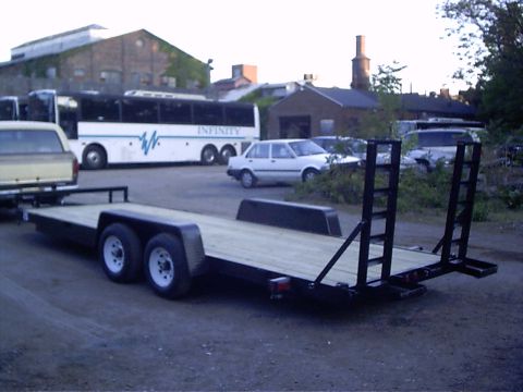 1979 Ford Bronco - A flatbed trailer is parked in a lot with a bus and several cars in the background.