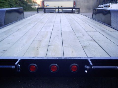 1979 Ford Bronco - Trailer loaded with a pickup truck in the background. The trailer has a wooden deck and three red lights.