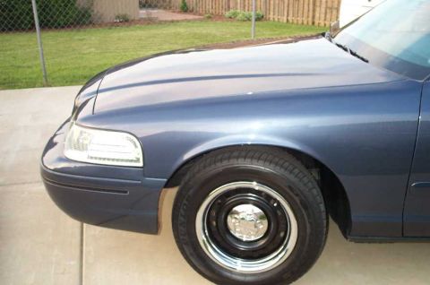 1998 Ford Crown Victoria - The front corner of a blue sedan is shown, parked on a concrete driveway with a grassy yard in the background.