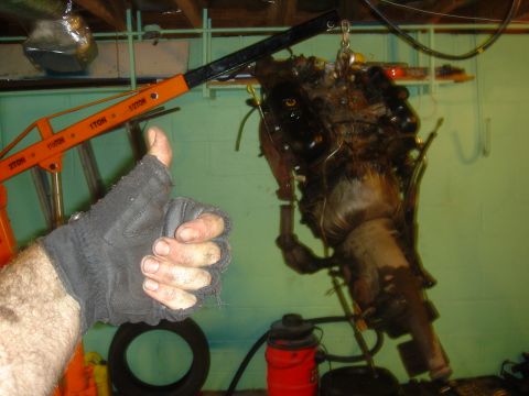 1986 Ford Mustang - An engine and transmission assembly is suspended by an engine hoist, with a hand giving a thumbs up in approval.