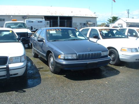 1999 Ford Crown Victoria - A blue sedan, likely a 1994 Chevrolet Caprice, is parked in an outdoor lot with other vehicles. The license plate reads E05627.